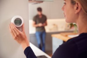 Woman adjusting her thermostat after a routine inspection.