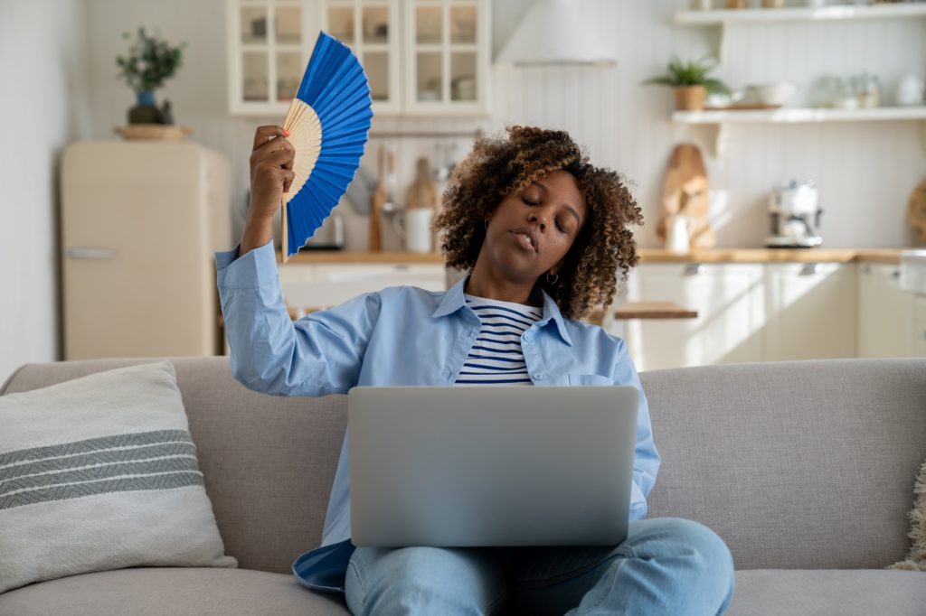 Tired African American millennial girl suffer from heat while working remotely from home
