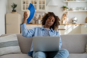 Tired African American millennial girl suffer from heat while working remotely from home